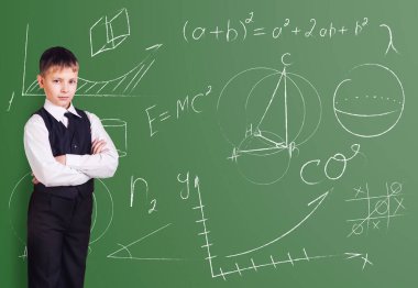 Little boy stands over blackboard background with formulas.