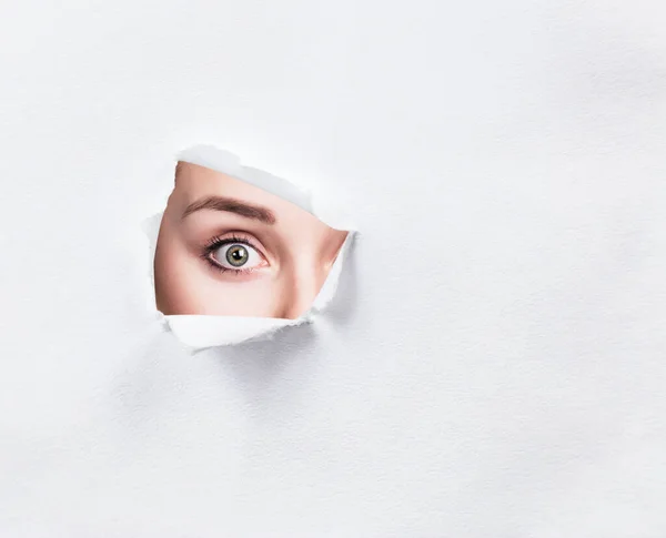 Surprised woman peeps into the slit of white paper. — Stockfoto