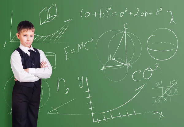 Little boy stands over blackboard background with formulas. — Stockfoto