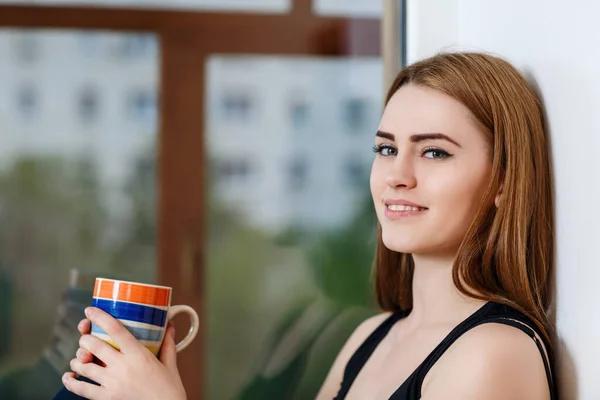 Jeune femme assise avec une tasse au rebord de la fenêtre à la maison dans les jours de pluie . — Photo