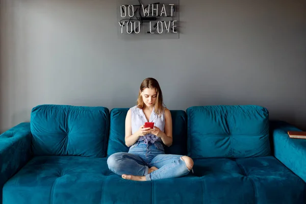 Jeune femme à la maison se détendre sur le canapé, en utilisant un smartphone . — Photo