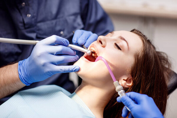 Dentist treating teeth to young woman patient in clinic.