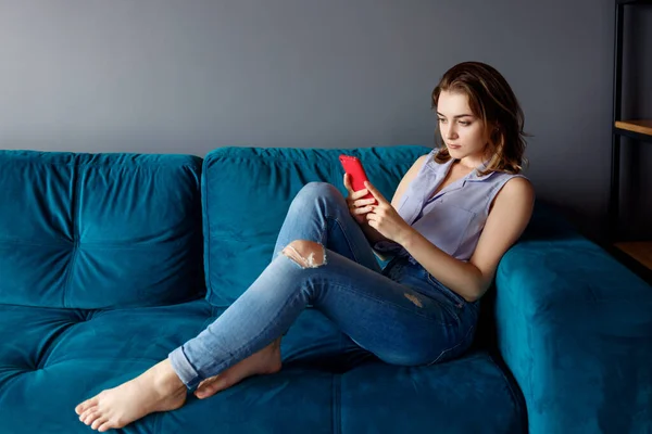 Ung kvinna hemma koppla av på soffan, med hjälp av smartphone. — Stockfoto
