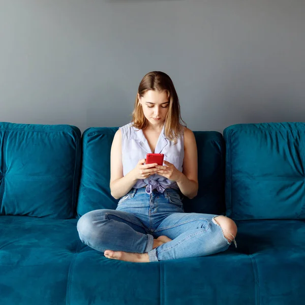 Ung kvinna hemma koppla av på soffan, med hjälp av smartphone. — Stockfoto