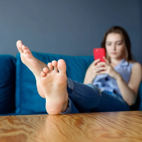 Ung kvinna hemma koppla av på soffan, med hjälp av smartphone. — Stockfoto