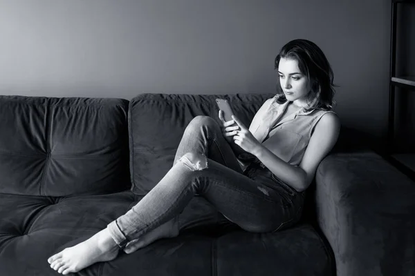 Ung kvinna hemma koppla av på soffan, med hjälp av smartphone. — Stockfoto