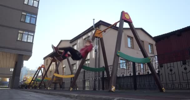 Mujer joven sonriente balanceándose en el columpio en el patio de recreo de la ciudad . — Vídeo de stock