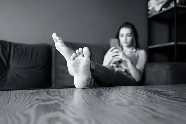Молода жінка вдома розслабляється на дивані, використовуючи смартфон . — стокове фото
