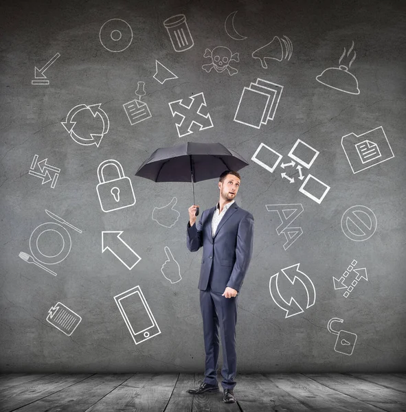 Businessman with umbrella over gray wall with icons background. — Stock Photo, Image