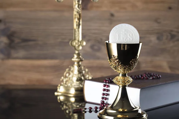 Catholic religion theme. The Cross, Holy Bible, rosary and golden chalice on wooden background.