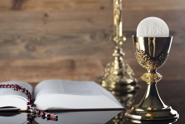 Catholic religion theme. The Cross, Holy Bible, rosary and golden chalice on wooden background.