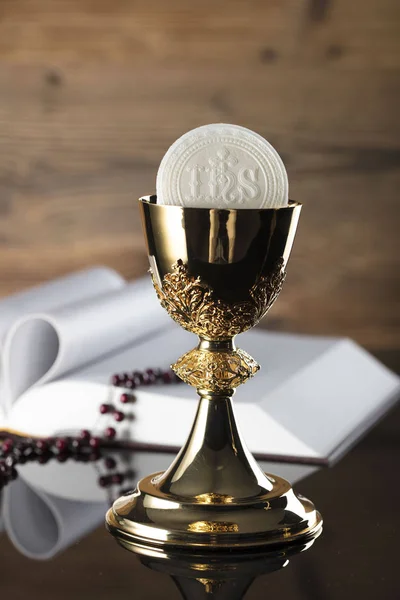 Catholic religion theme. Holy Bible, rosary and golden chalice on wooden background.