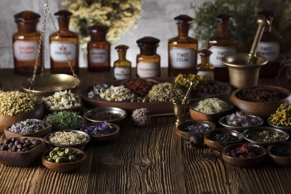 Natural medicine background. Brass mortar, bottles. Rustic table. Assorted dry herbs in bowls. Bokeh.