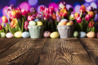Paskalya arka plan. Rustik ahşap masa. Lale ve bahar çiçekleri. Paskalya yumurtaları. Renkli bokeh. Tipografi için yer.