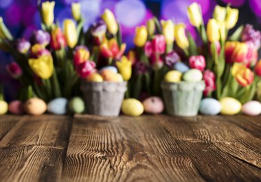 Paskalya arka plan. Rustik ahşap masa. Lale ve bahar çiçekleri. Paskalya yumurtaları. Renkli bokeh. Tipografi için yer.