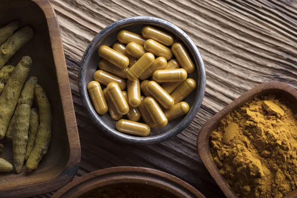 Curcuma capsules, turmeric roots and powder in bowls. Anti cancer medicine. Wooden table. Top view shot.