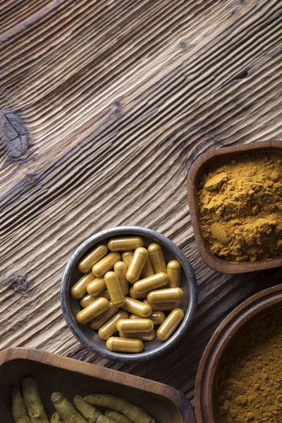 Curcuma capsules, turmeric roots and powder in bowls. Anti cancer medicine. Wooden table. Top view shot.