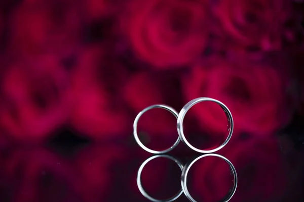 Engagement rings and red roses background. Romantic concept.