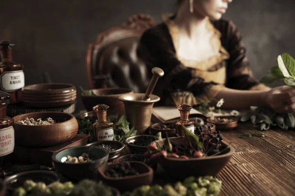 Natural medicine concept. Vintage pharmacist preparing natural medicament. Brass mortar and  bottles. Rustic table. Assorted dry herbs in bowls.