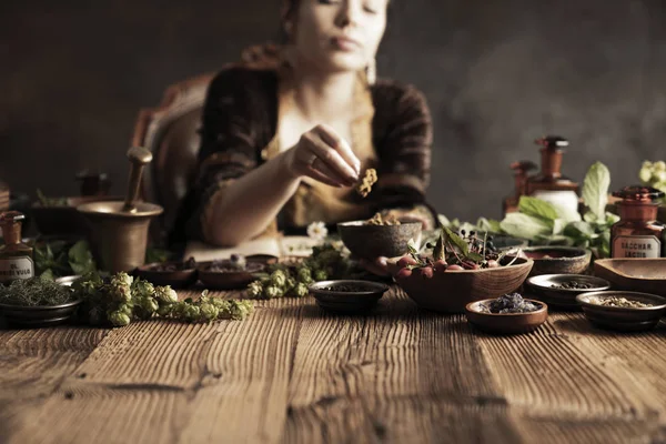 Natural medicine concept. Vintage pharmacist preparing natural medicament. Brass mortar and  bottles. Rustic table. Assorted dry herbs in bowls.