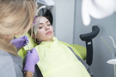 Diş hekimliği. Dişçi, dişçi kliniğindeki kadın hastayı muayene ediyor. Modern tıbbi ekipman.