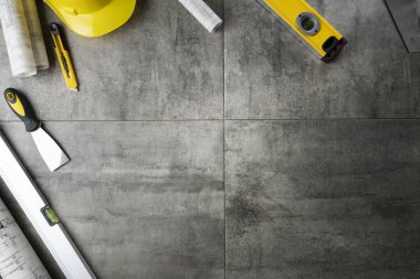 Müteahhit konsepti. Müteahhidin alet çantası: sarı başlık, karalama, el testeresi ve gri fayansların arkasındaki defter..