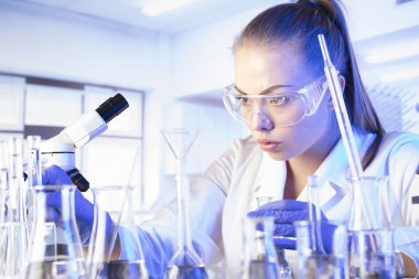 Laboratuvar içi. Bilim araştırma konsepti. Deney sırasında genç bir bilim adamı modern laboratuvarda mikroskop kullanıyor. Cam tüpler ve beherler..