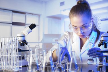 Laboratuvar içi. Bilim araştırma konsepti. Deney sırasında genç bir bilim adamı modern laboratuvarda mikroskop kullanıyor. Cam tüpler ve beherler..