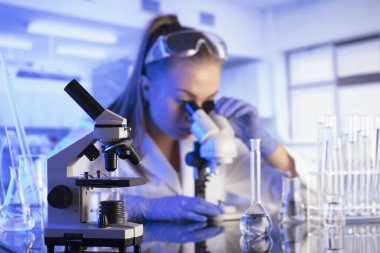 Laboratuvar içi. Bilim araştırma konsepti. Deney sırasında genç bir bilim adamı modern laboratuvarda mikroskop kullanıyor. Cam tüpler ve beherler..