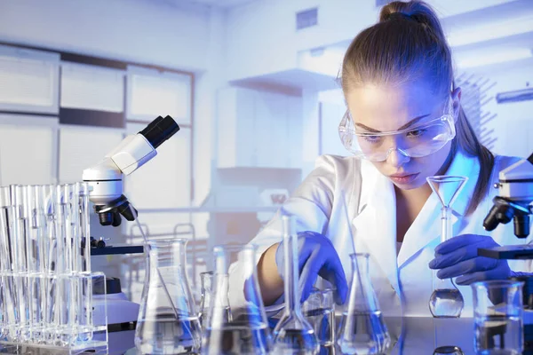 Laboratuvar içi. Bilim araştırma konsepti. Deney sırasında genç bir bilim adamı modern laboratuvarda mikroskop kullanıyor. Cam tüpler ve beherler..