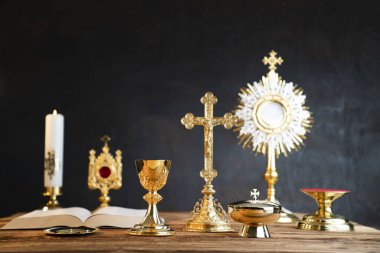 Katolik dini kavramı. Katolik sembolleri kompozisyonu. Haç, Monstrance, Kutsal İncil ve altın kadeh ahşap sunak ve gri arka plan. 