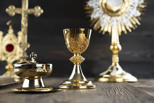 Catholic religion concept. Catholic symbols composition. The Cross, monstrance,  Holy Bible and golden chalice on wooden altar and gray background.