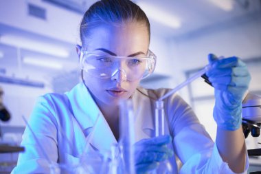 Bilim araştırma konsepti. Deney sırasında genç bir bilim adamı modern laboratuvarda mikroskop kullanıyor. Cam tüpler ve beherler..