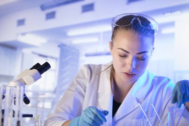 Bilim araştırma konsepti. Deney sırasında genç bir bilim adamı modern laboratuvarda mikroskop kullanıyor. Cam tüpler ve beherler..