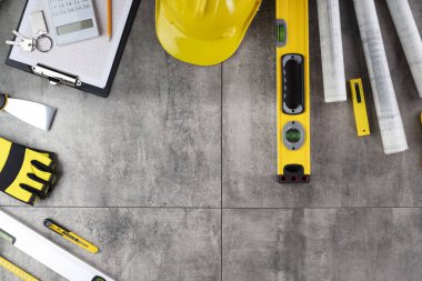 Müteahhit konsepti. Müteahhidin alet çantası, sarı başlık, libella, el testeresi. Gri karoların arka planındaki planlar ve defterler.