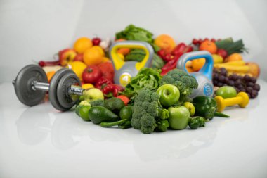 Fitness konsepti. Sağlıklı beslenme: meyve ve sebze. Spor aletleri: tartı makinesi ve dambıllar. Beyaz arkaplan.