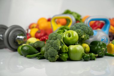 Fitness konsepti. Sağlıklı beslenme: meyve ve sebze. Spor aletleri: tartı makinesi ve dambıllar. Beyaz arkaplan.