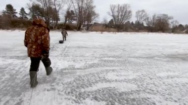 Big river in the winter. Fishermen go on flat ice. Sleds with gear are dragged over the ropes. Far horizon, clean air.