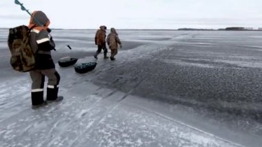 Big river in the winter. Fishermen go on flat ice. Sleds with gear are dragged over the ropes. Far horizon, clean air.