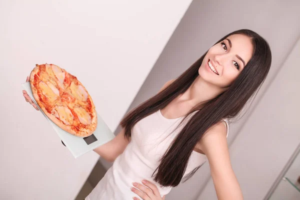 Régime alimentaire. Jeune belle fille pesant balance tenant pizza. Le concept de saine alimentation et l'obésité. Belle silhouette mince fille. Nourriture malsaine. Mode de vie. Perte de poids. Obésité — Photo
