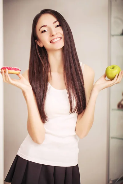 Régime alimentaire. Une jeune femme tenant une pizza sur la balance et faisant un choix entre une pomme et un beignet. Le concept de saine alimentation — Photo