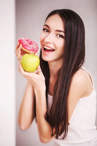 Régime alimentaire. Une jeune femme tenant une pizza sur la balance et faisant un choix entre une pomme et un beignet. Le concept de saine alimentation — Photo