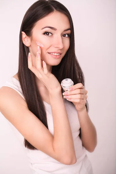 Bellezza, persone, cosmetici, cura della pelle e concetto di salute - felice sorridente giovane donna applicando crema al suo viso — Foto Stock