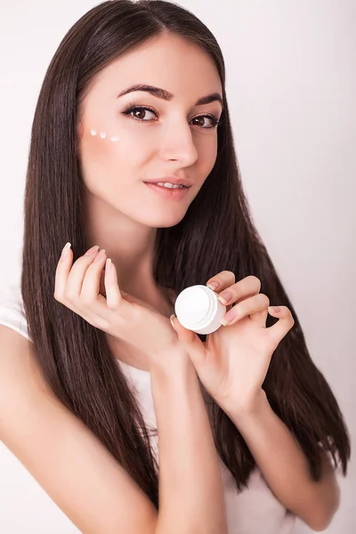 Bellezza, persone, cosmetici, cura della pelle e concetto di salute - felice sorridente giovane donna applicando crema al suo viso — Foto Stock
