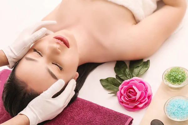 Spa, beauty, people and body care concept - красивая женщина, получающая лечение лица на праздничном световом фоне — стоковое фото