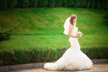 Bir güzel şehvetli genç esmer gelin uzun beyaz gelinlik ve ormandaki buket doğal arka planda, yatay resim açık tutarak ayakta peçe tam uzunlukta yan görünüm