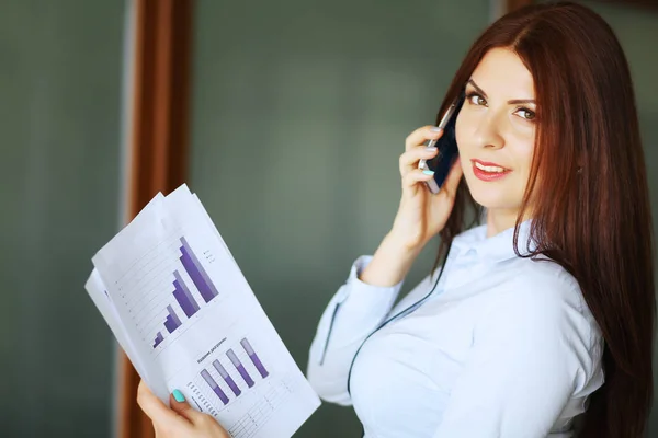 Affärskvinna talar på mobiltelefon, leende och tittar på kameran. Kort skärpedjup. — Stockfoto