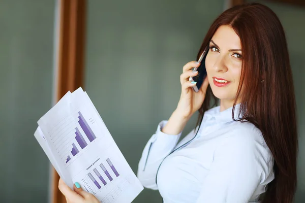 Business woman talking on mobile phone, smiling and looking at camera. Shallow depth of field. — Stock Photo, Image