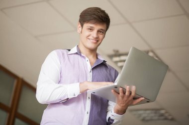 ofiste duran dizüstü kullanan genç iş adamı