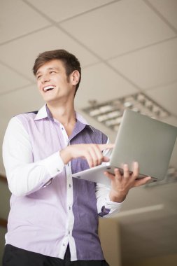 Genç adam holding dizüstü gülümseyen ve tekrar ayakta iken yazarak